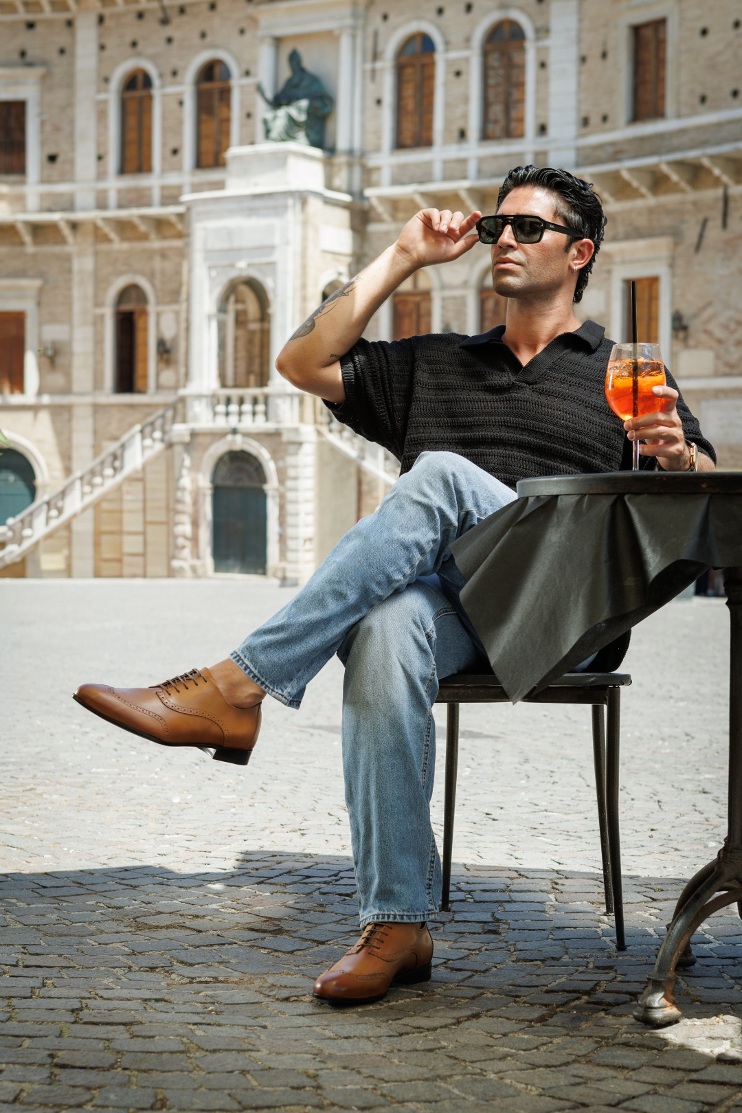 Nunzio Orsini light brown wingtip Oxford shoes worn at a café table in a Marche, Italy piazza with Aperol Spritz