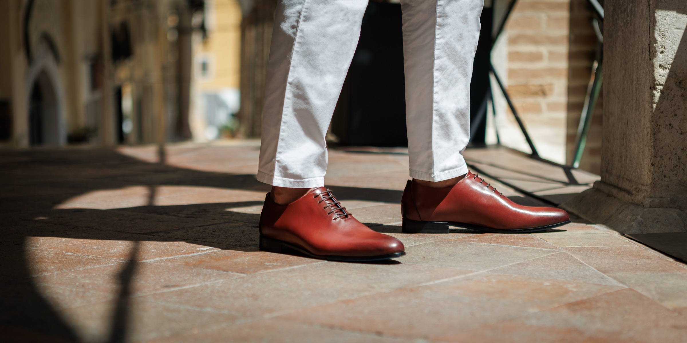 Nunzio Orsini whole-cut Oxfords in maroon leather, worn on a sunlit stone portico