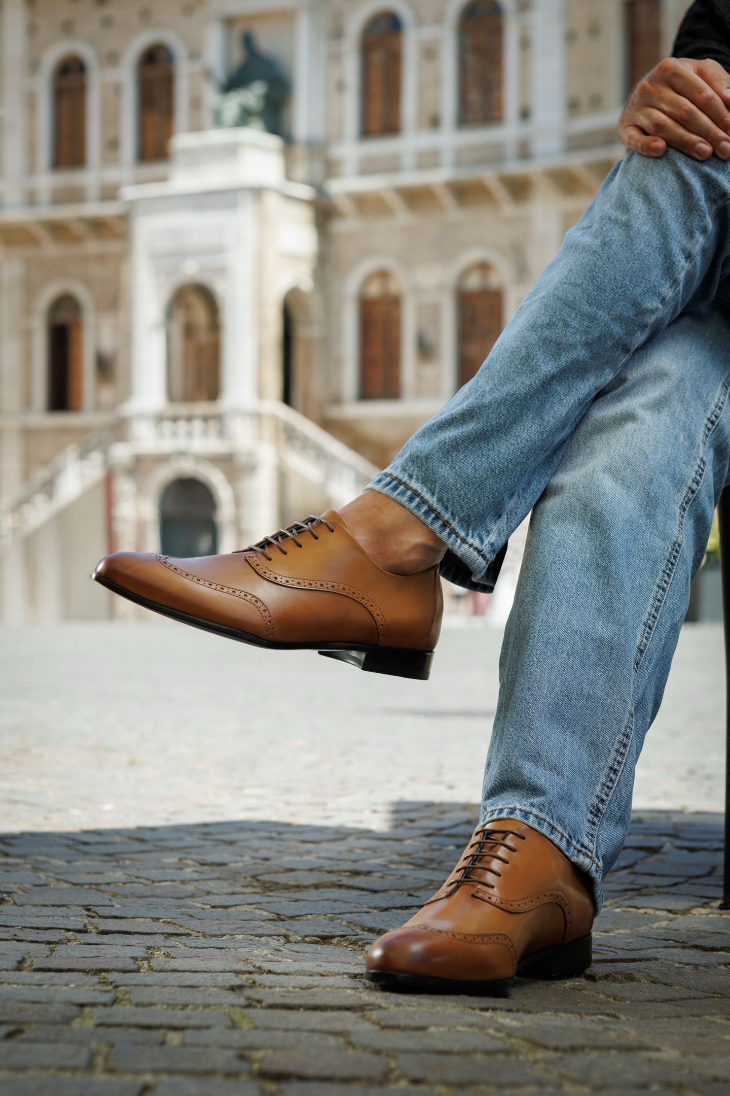 The Giuseppe wingtip Oxford in light brown, worn with denim in an Italian piazza